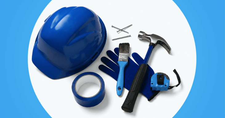 Capacete azul, luvas, martelo e outras ferramentas dispostas sobre uma superfície de trabalho.
