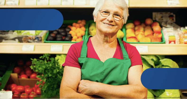 Mulher usando avental verde ao lado de uma estante cheia de diversos vegetais.