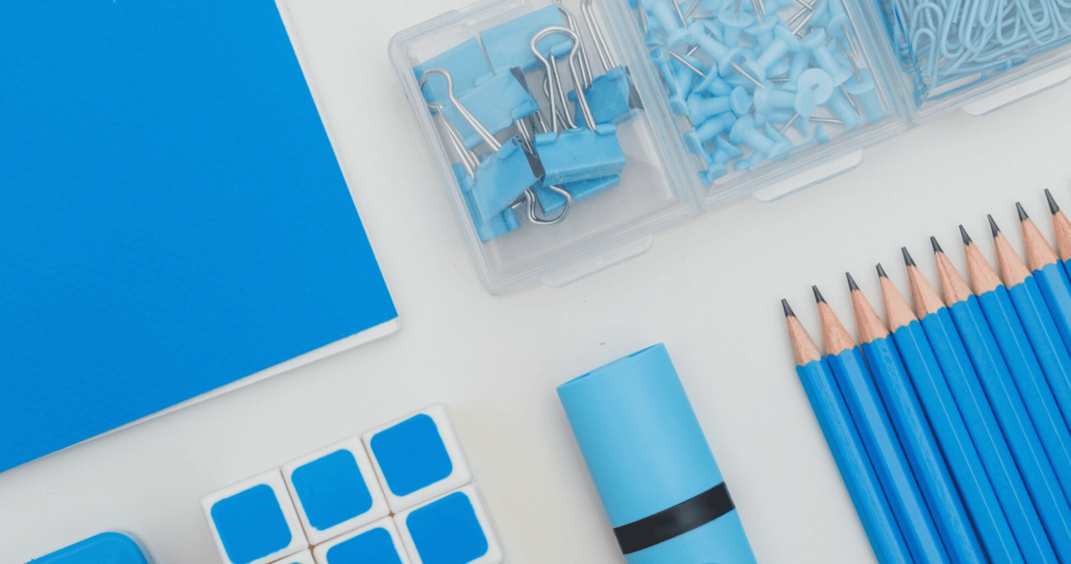 material escolar azul organizado com lápis, clipes, tachinhas e papel sobre fundo branco.