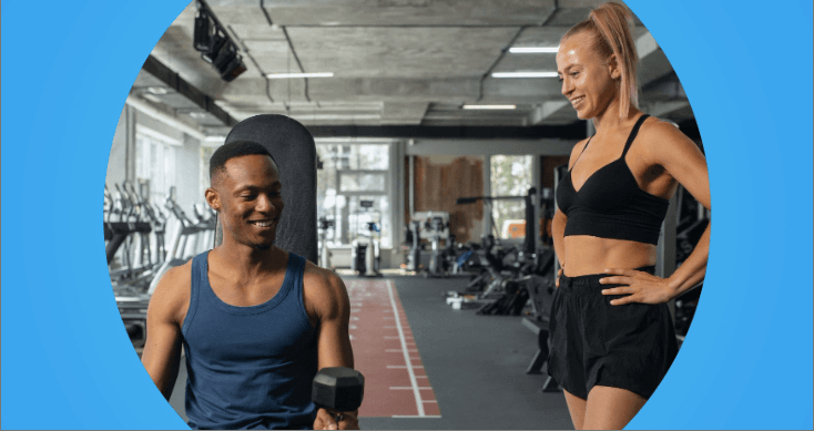 Pessoa sentada em uma academia com aparelhos ao fundo, com personal trainer ao lado.