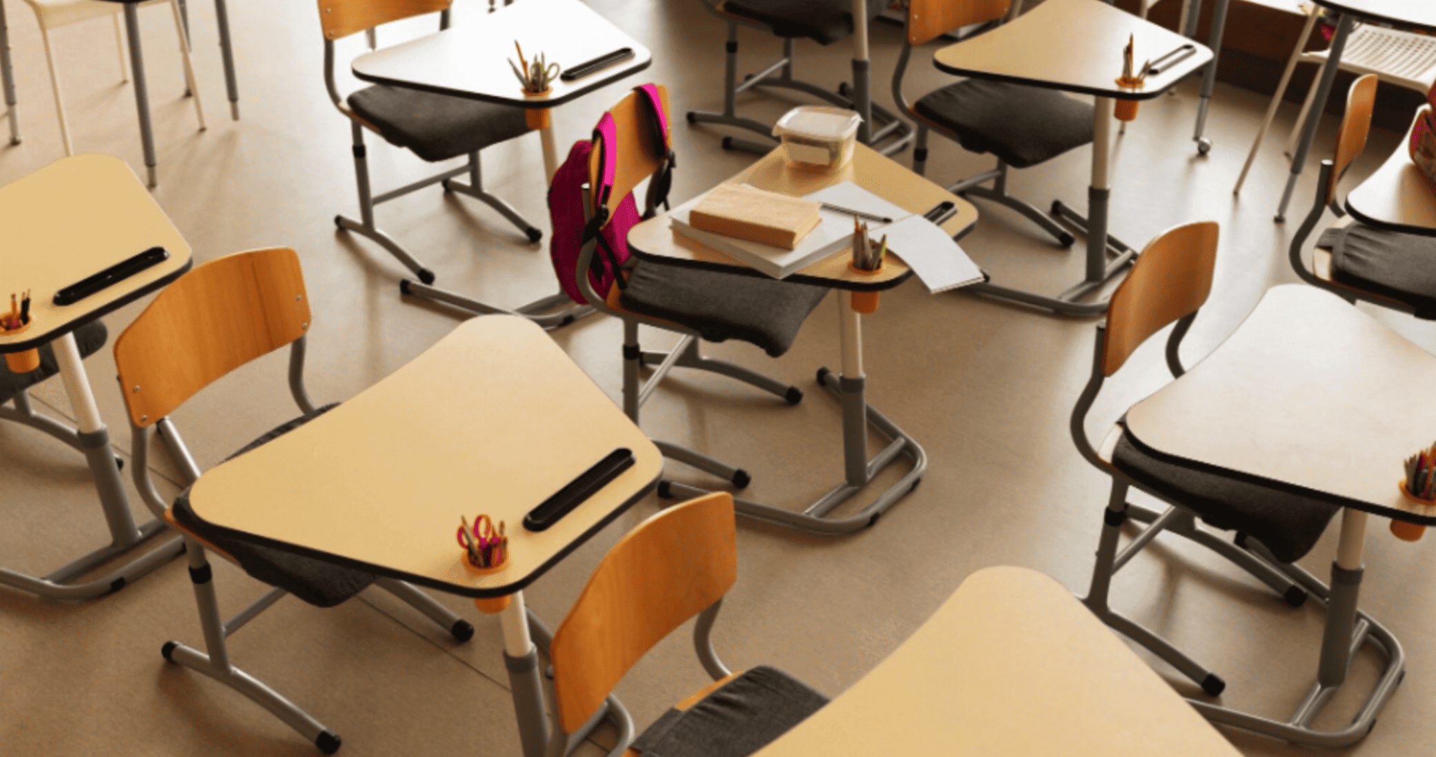 carteiras escolares vazias vistas de cima com mochila rosa e livros sobre uma delas.