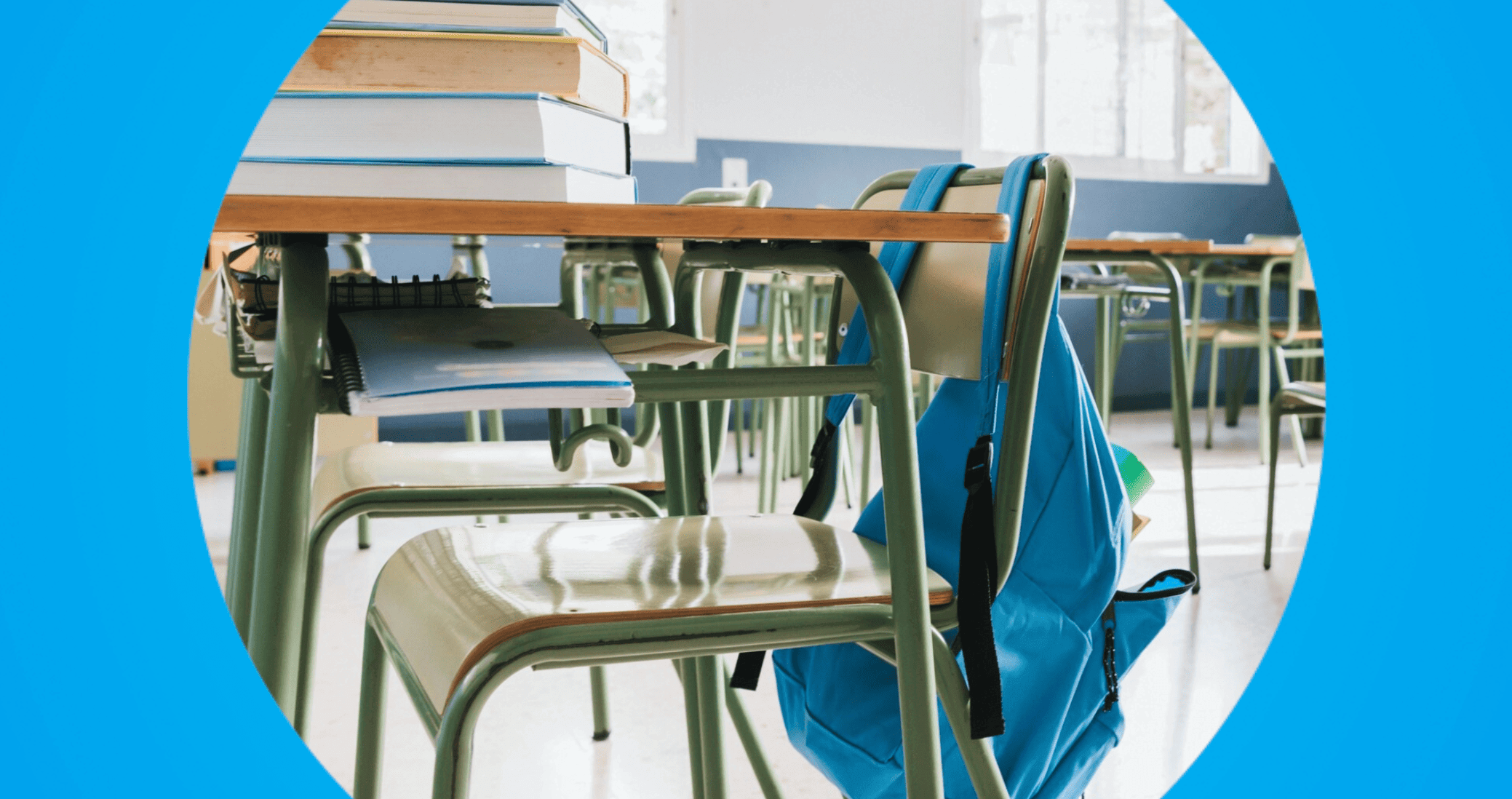 sala de aula vazia com carteiras, livros empilhados e mochila azul pendurada na cadeira.