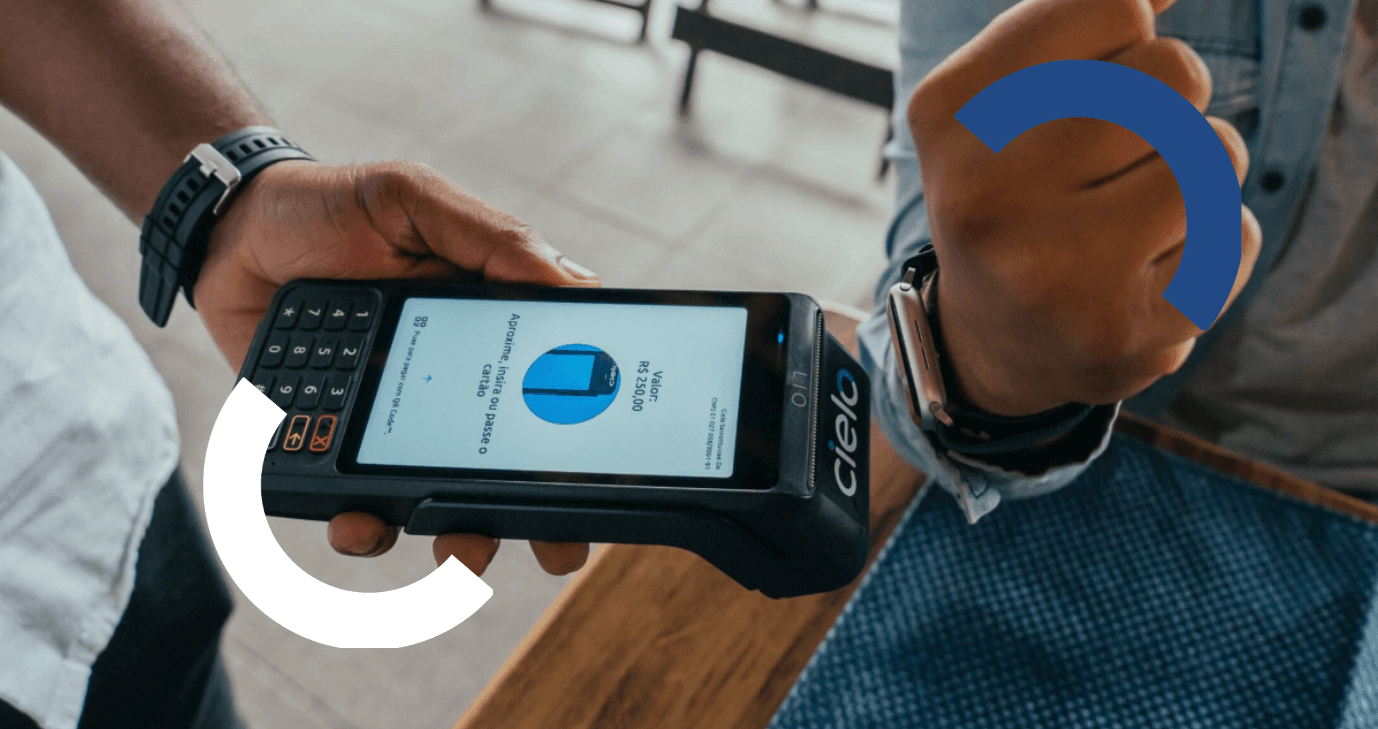 Uma pessoa realizando um pagamento por aproximação com smartwatch em uma maquininha da Cielo, enquanto o visor do aparelho exibe o valor da transação.