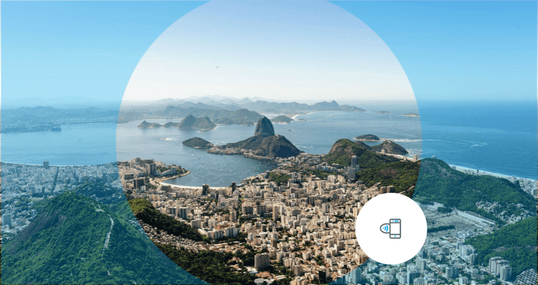 A imagem mostra uma vista panorâmica aérea do Rio de Janeiro, destacando a Baía de Guanabara, o Pão de Açúcar e a cidade ao redor sob um céu azul.