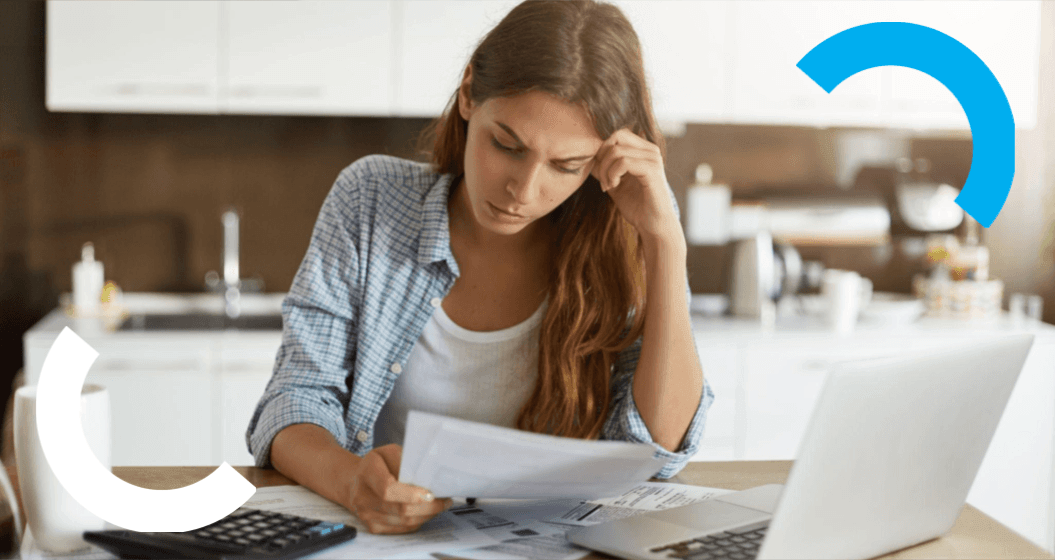 Mulher sentada à mesa em casa, usando computador e analisando documentos, com expressão de preocupação e um ícone de atualização ou retorno em forma de seta azul ao lado, sugerindo revisão de informações.