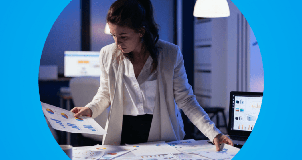 Mulher analisando relatórios financeiros e gráficos em escritório, organizando dados e indicadores para gestão empresarial.
