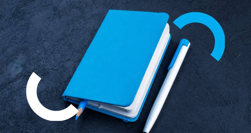 Caderno azul e caneta dispostos sobre uma superfície.