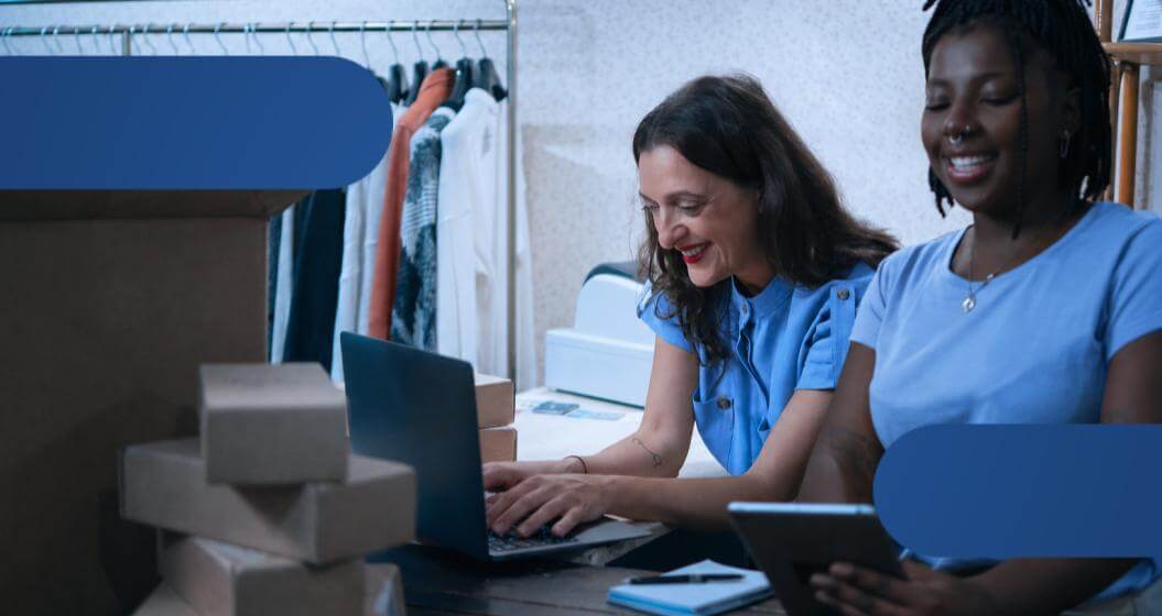 Duas mulheres trabalhando em um escritório, uma usando um laptop e a outra um tablet.
