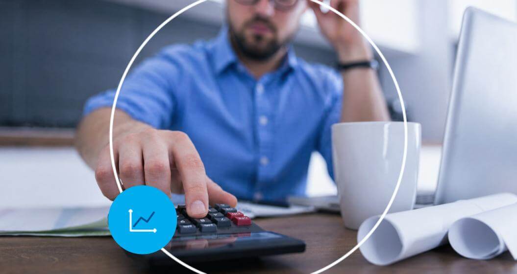 Pessoa usando uma calculadora em uma mesa de trabalho com notebook, papéis e caneca.