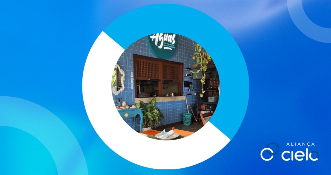 Interior do Restaurante das Águas na Bahia, com cozinha à vista, paredes de azulejos azuis, decoração com plantas e ambientação acolhedora. A foto está sobre fundo azul com grafismos institucionais com elementos gráficos da identidade do Aliança Cielo.