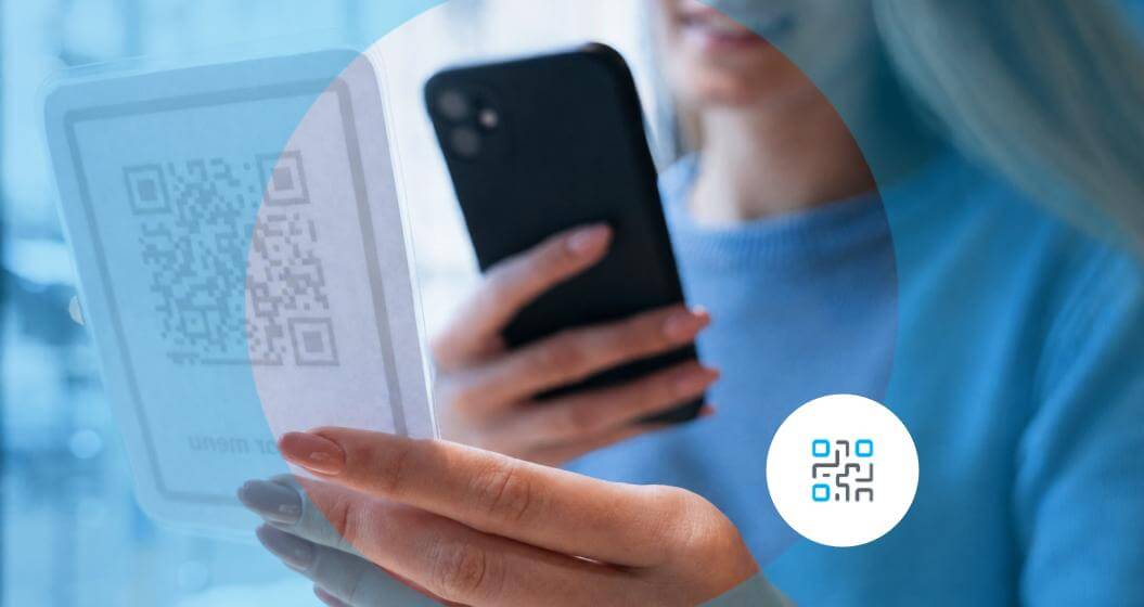 Pessoa utiliza o celular para escanear um QR Code exibido em um suporte transparente, realizando um pagamento digital.