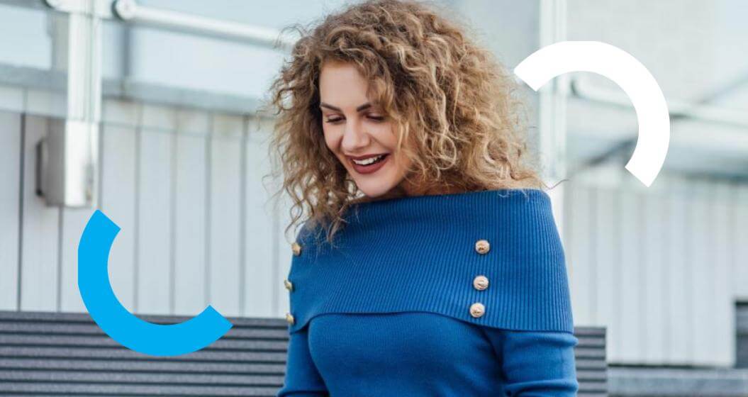 Mulher de cabelos cacheados e blusa azul com botões dourados sorri enquanto olha para baixo. Ao fundo, há uma escadaria e a fachada de um prédio, com elementos gráficos em formato de arcos nas cores azul e branca sobre a imagem.