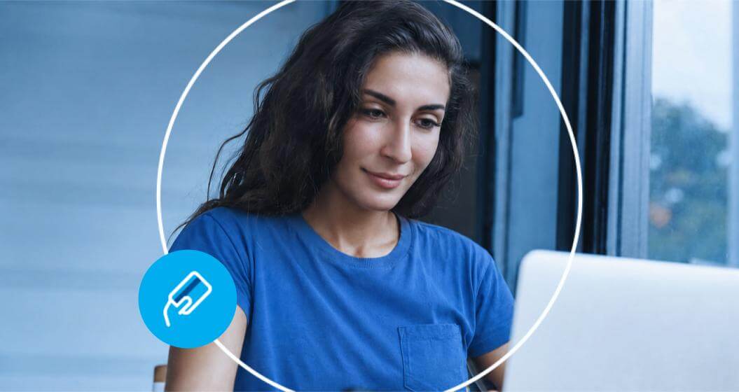 Mulher de cabelos escuros e camiseta azul foca a atenção na tela de um notebook.