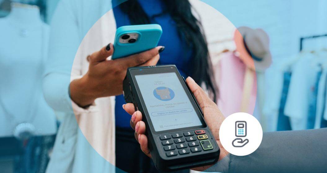 Cliente realizando um pagamento por aproximação com uma maquininha Cielo, enquanto segura um smartphone. Ao fundo, uma atendente acompanha a transação em um ambiente comercial. Ícone de pagamento por aproximação destacado no canto inferior direito da imagem.