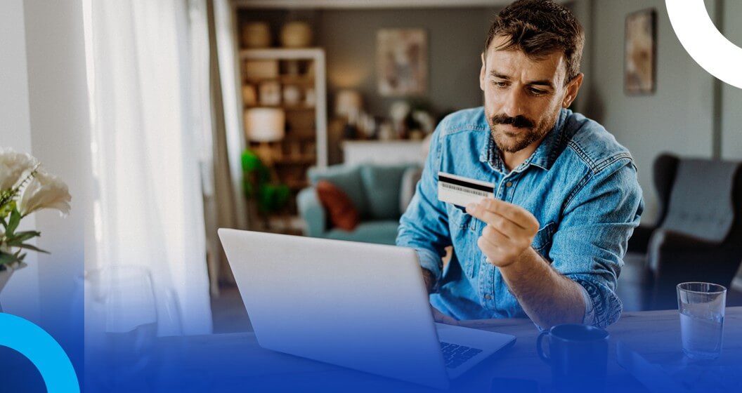 Pessoa utilizando notebook em casa enquanto segura um cartão de pagamento para realizar uma compra online, ilustrando comportamento do consumidor no e-commerce e pagamentos digitais.