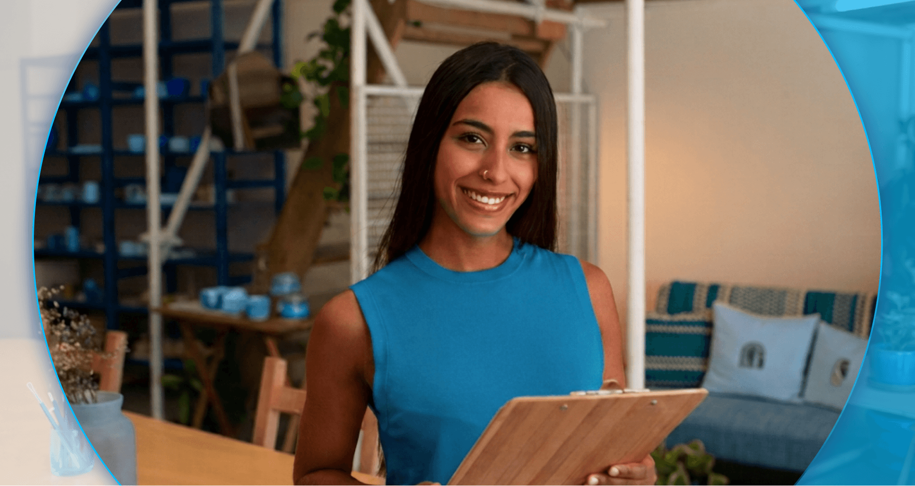 Mulher jovem de cabelos longos escuros sorri enquanto segura uma prancheta de madeira. Ela veste uma blusa regata azul-turquesa em um ambiente decorado, com enquadramento circular sobre fundo azul.